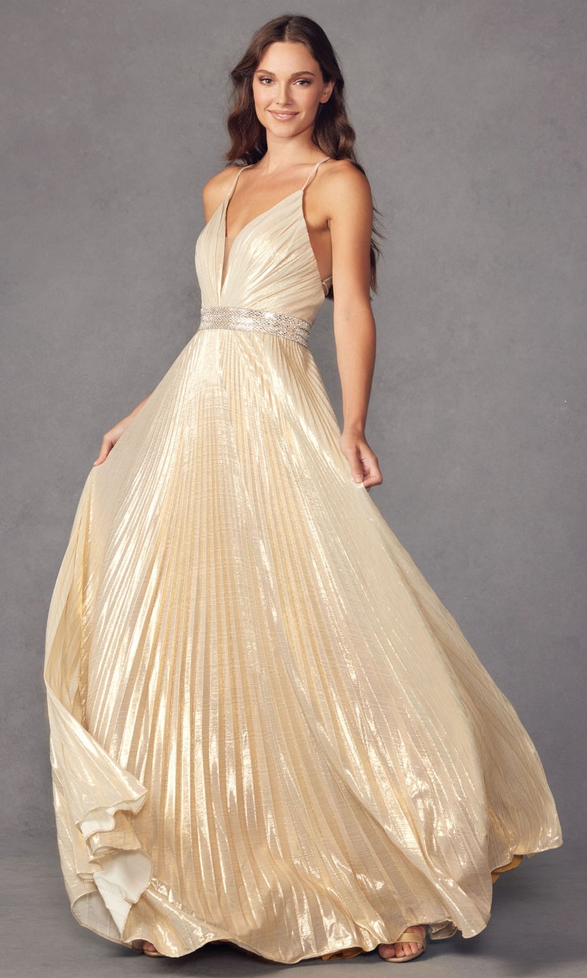 A woman wears the Deep V-Neck Pleated Long A-Line Prom Dress 226, a gold metallic floor-length gown with spaghetti straps and a rhinestone belt, posed against a plain grey background.